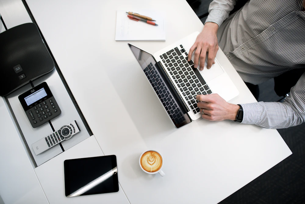 Een persoon werkt aan een laptop op een bureau met een telefoon